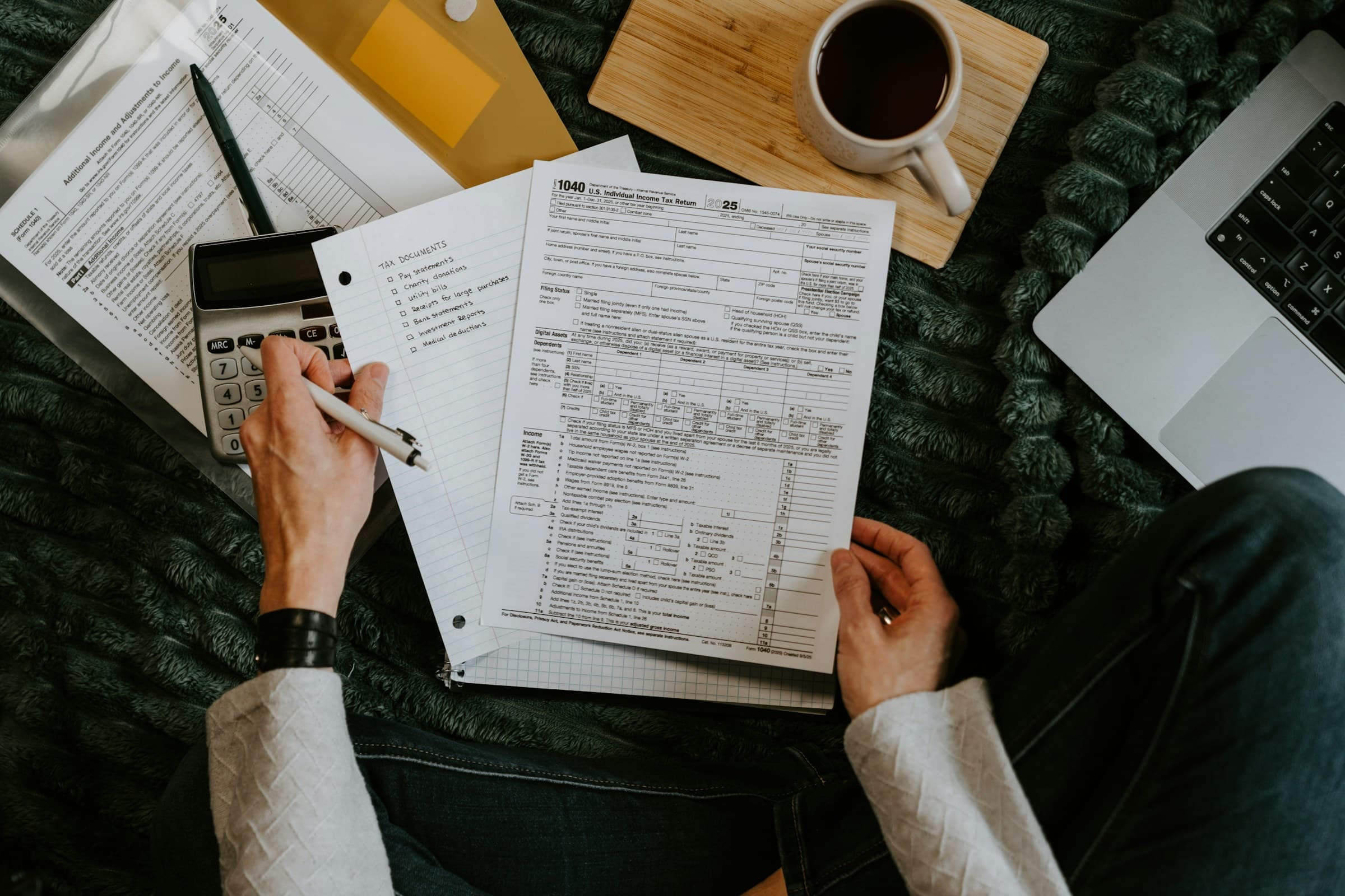 A person at home going through tax papers with a pen, a calculator and a cup of coffee.